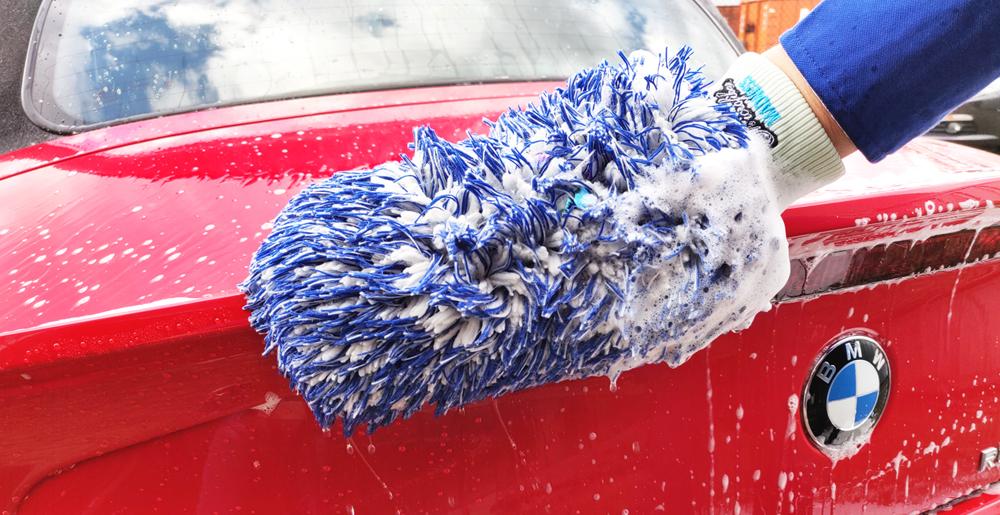 Persoon brengt autoshampoo met wax aan op een rode BMW met behulp van een washandschoen